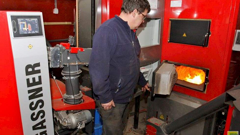 Tienus Berkepies controleert de houtkachel. Met deze kachel, een houtgestookte cv-ketel van Hargassner, verwarmt hij de pluimveestallen, het akkerbouwbedrijf, zijn woning en de leeskamer. Bovendien levert deze kachel voldoende warmte om zijn aardappelen t