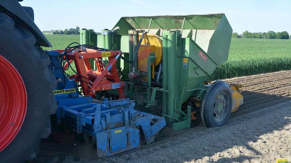 Achter de trekker hangt een bontgekleurd treintje van een Rabe kopeg (blauw), een oude vierrijige Hassia pootmachine (groen) en een oude maïszaaimachine van Kleine (geel).