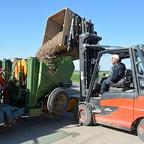 De zon schijnt fel als Westerdijk een tonskist met aardappelen leegstort in de pootcombinatie die op het erf staat.